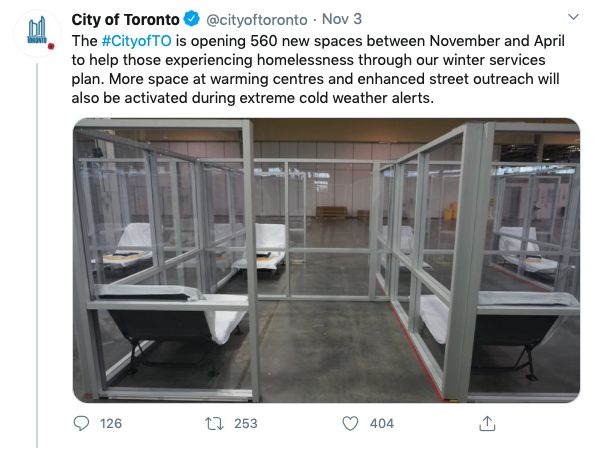 A screen shot of a tweet by @cityoftoronto. It reads, "The City of Toronto is opening 560 new spaces between November and April to help those experiencing homelessness through out winter services plan. More space at warming centres and enhanced street outreach will also be activated during extreme cold weather alerts." There is also an imge which shows a large, warehouse like room in which glass barriers separate cots. The rooms are about twice the size of the cots. The glass walls provide no privacy. The cots resemble lawn chairs and feature a thin mattress.